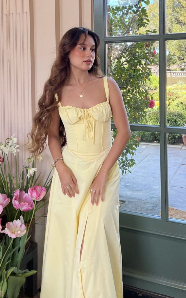 Woman in a yellow gown standing in a bright room with plants.